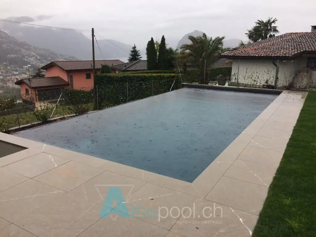 Piscina interrata con bordo a sfioro, in giardino con vista sulle montagne e piante tropicali.