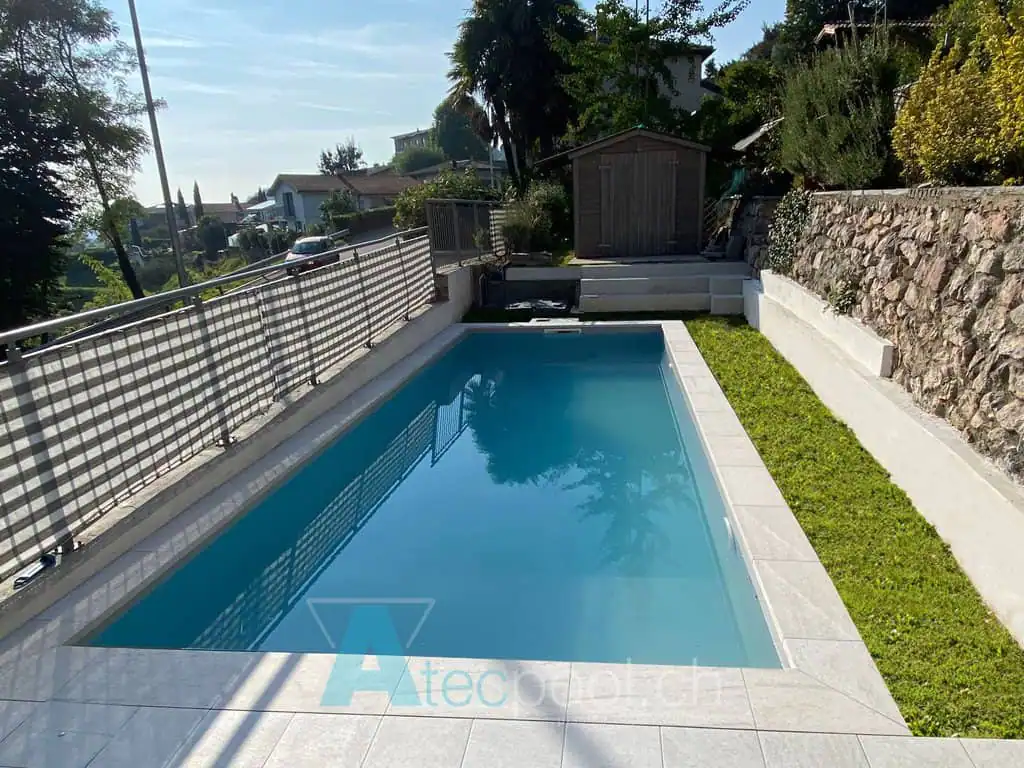 Piscina interrata con bordo piastrellato e giardino circostante, ambiente tranquillo e rilassante all'aperto.