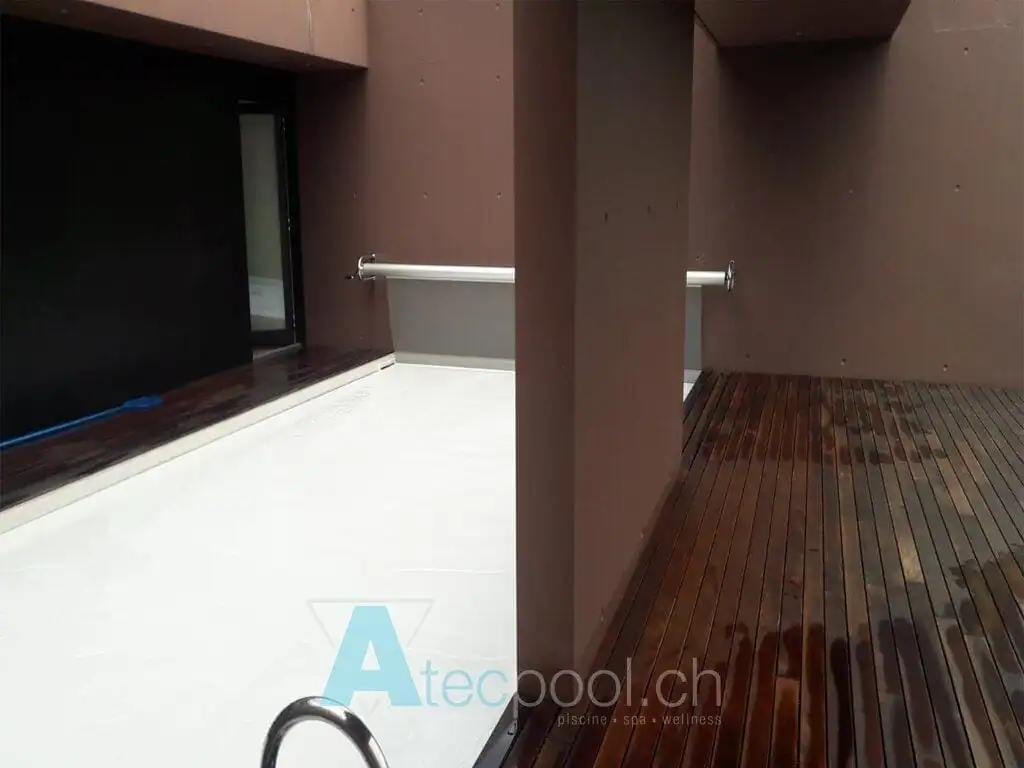 Piscina interrata a sfioro con bordo in mosaico scuro e area relax in legno, ideale per wellness e relax.