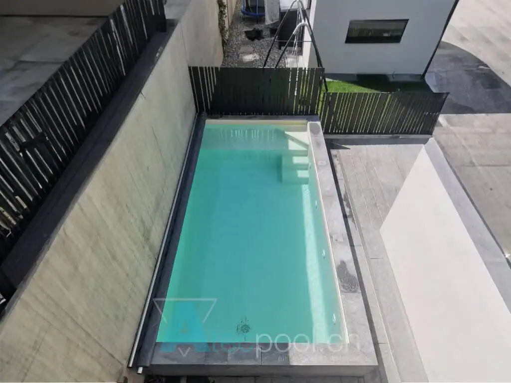 Piscina interrata con bordo a sfioro in un cortile privato, circondata da recinzione in legno e pavimentazione moderna.