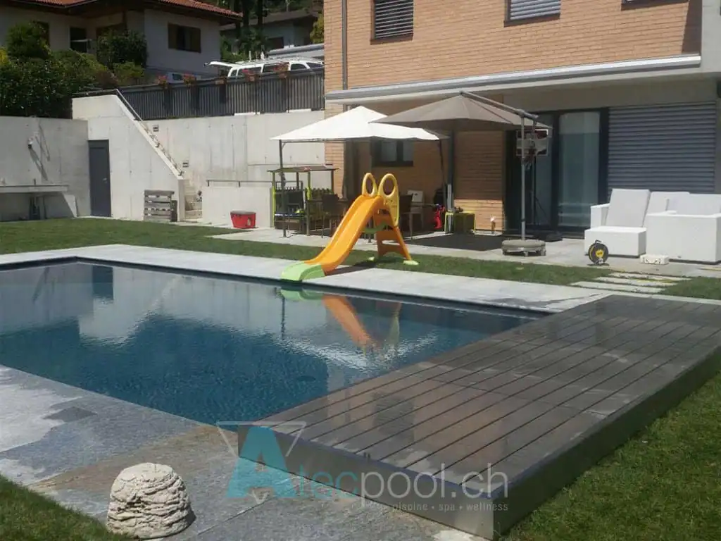Piscina interrata con bordo a sfioro e area giochi per bambini con scivolo giallo. Zona relax con ombrelloni e mobili da esterno, ideale per il benessere e il divertimento all'aperto.