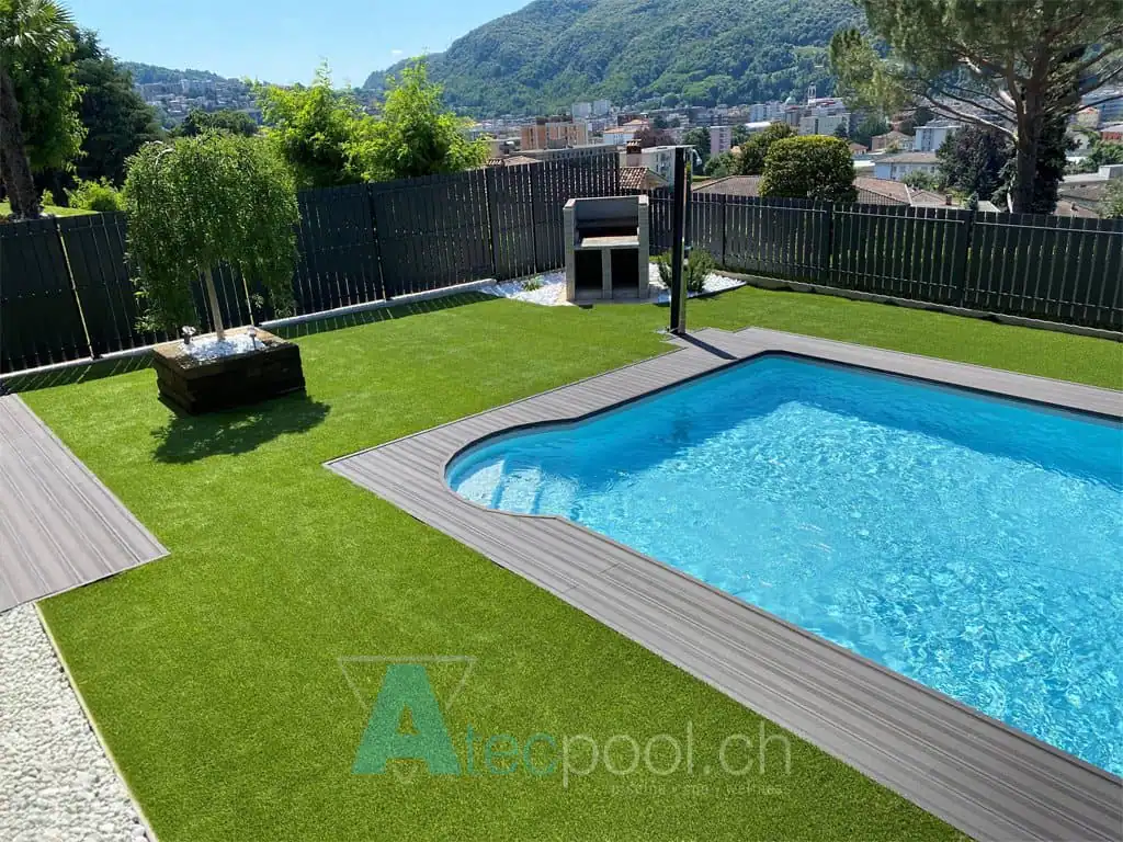 Piscina interrata con bordo sfioro, immersa in un giardino ben curato con alberi e piante ornamentali, offre un ambiente rilassante in una zona panoramica di montagna.