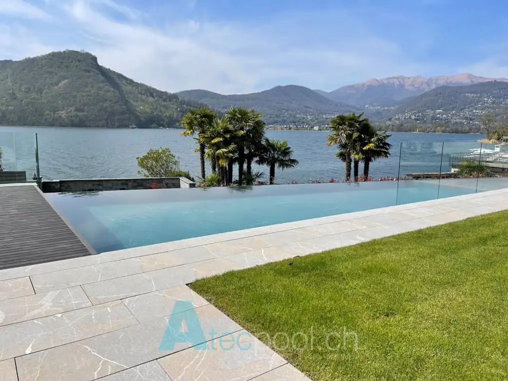 Relaxing infinity pool with panoramic lake view surrounded by lush greenery and mountains in Ticino.