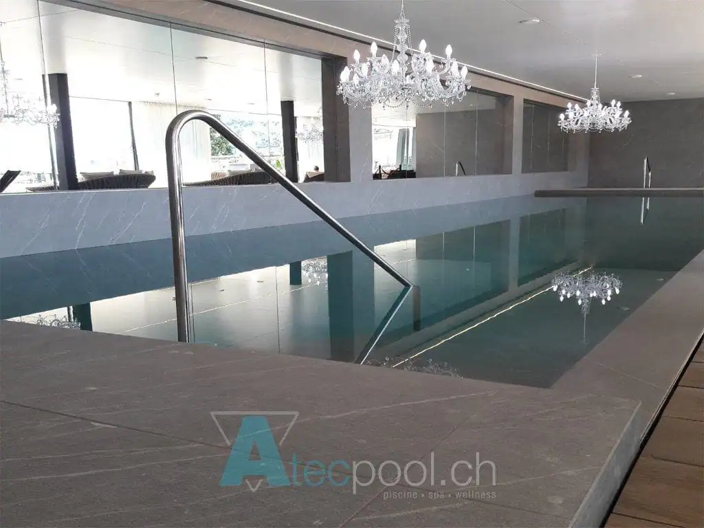 Piscina coperta a sfioro con scala in acciaio, elegante ambiente wellness con lampadari chandeliers.