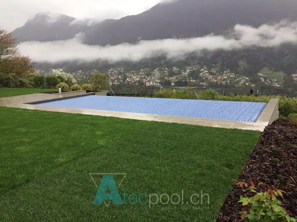 Piscina interrata con rivestimento in fibra sintetica, immersa nel verde con vista sulle montagne e paesino in lontananza.