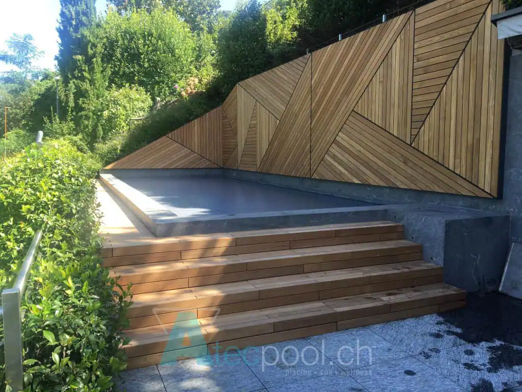 Piscina interrata con rivestimento in legno e scalinate in teak, ambientata in un giardino verde con terrazza in pietra. Design moderno e naturale, perfetta per relax e benessere all'aperto.