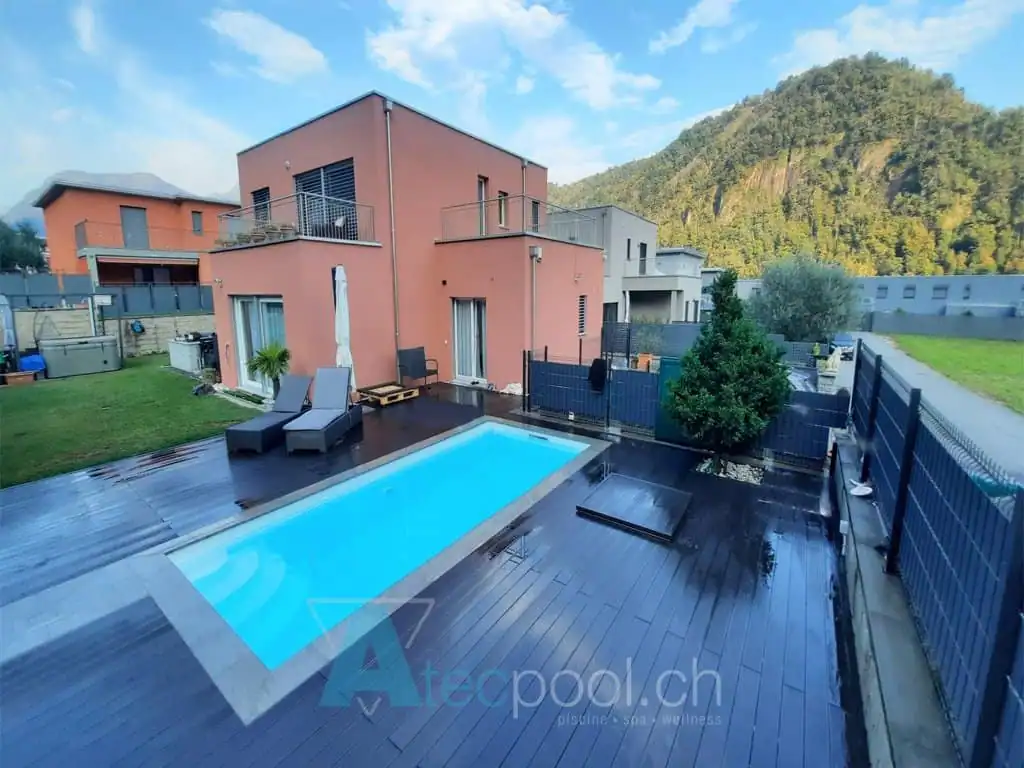 Piscina interrata con rivestimento in legno, situata nel cortile di una moderna abitazione con vista sul verde montano.