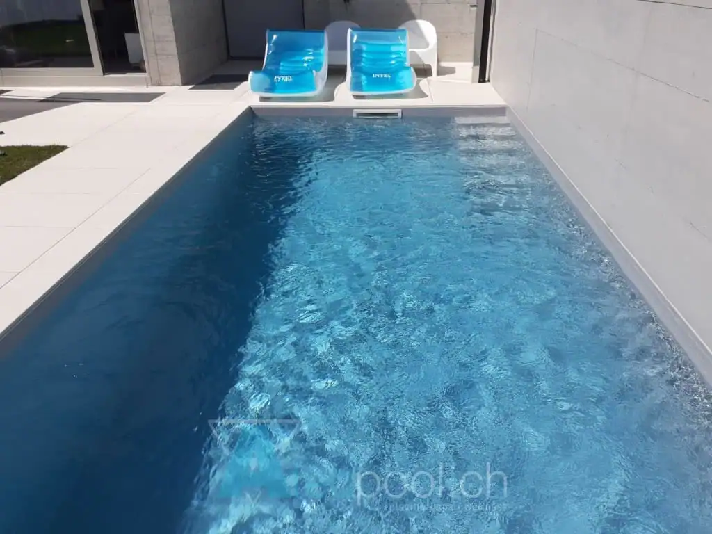 Piscina interrata a sfioro con acqua blu cristallina e area relax con lettini a bordo vasca.
