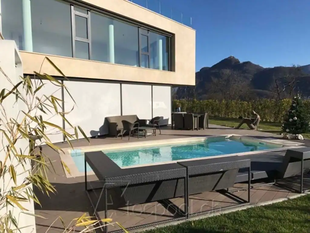 Piscina interrata con bordo a sfioro, situata in giardino con vista montagna e arredamento moderna. Perfetta per relax e svago all'aperto in un contesto naturale.