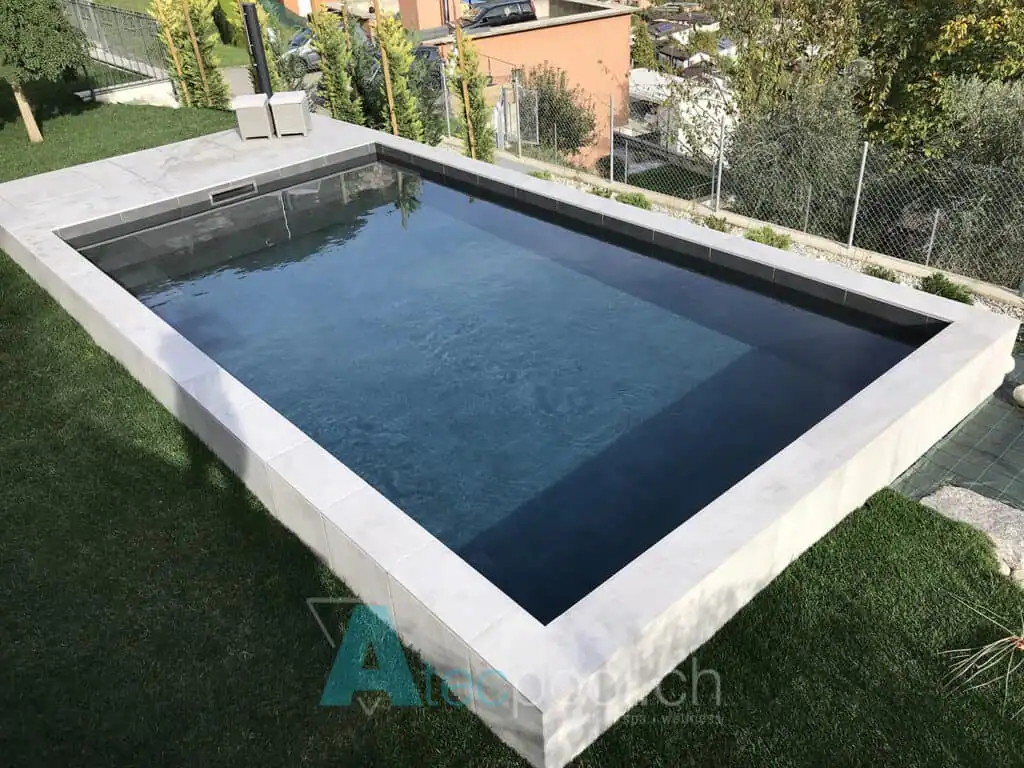 Piscina interrata con rivestimento in pietra, circondata da un prato verde e con vista sulla città.