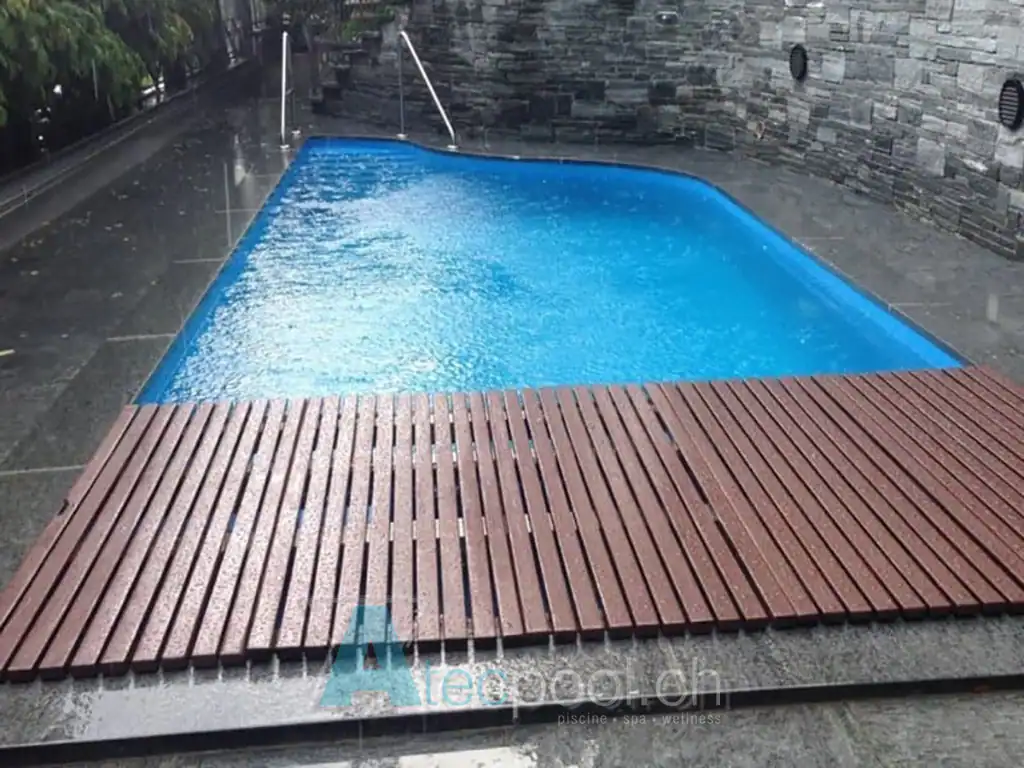 Piscina interrata con bordo a sfioro, rivestimento in piastrelle blu e pavimento in legno, ideale per relax e wellness.