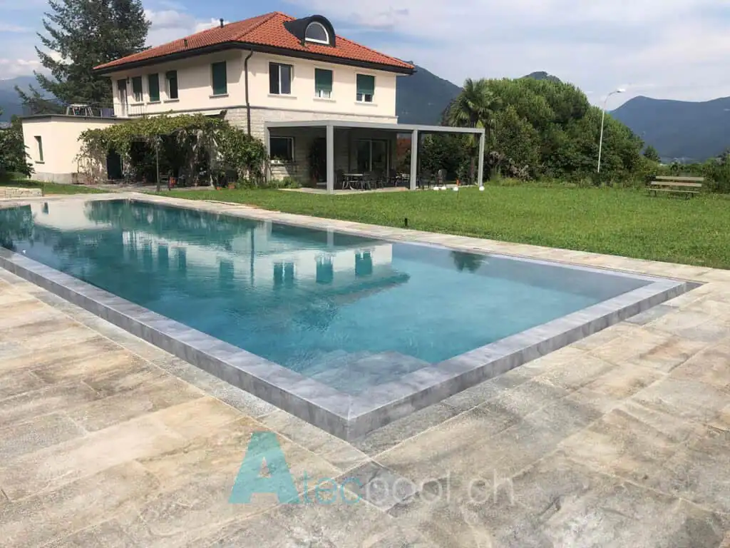 Piscina interrata con finitura in pietra naturale, situata in un giardino con vista montagna. Ideale per relax e svago all'aperto in ambienti privati.