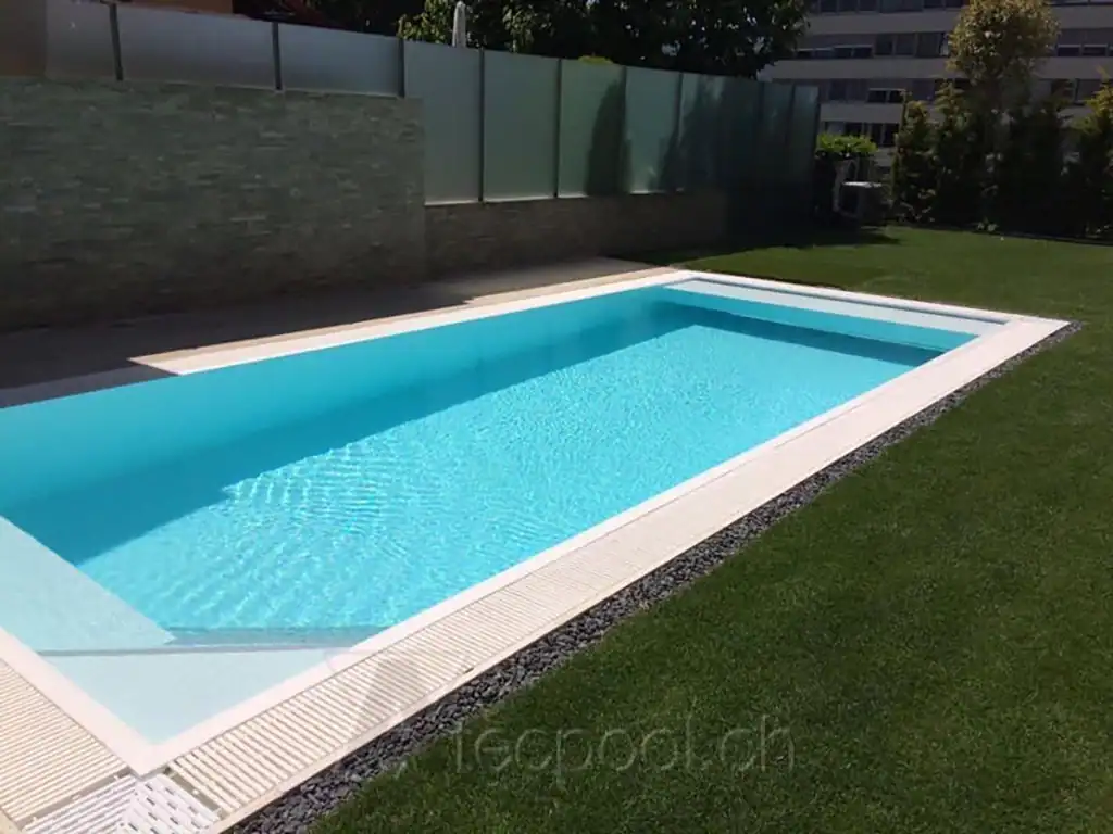 Piscina interrata a sfioro con riflessi d'acqua azzurra, circondata da prato verde e recinzione moderna. Ideale per il relax all'aperto.