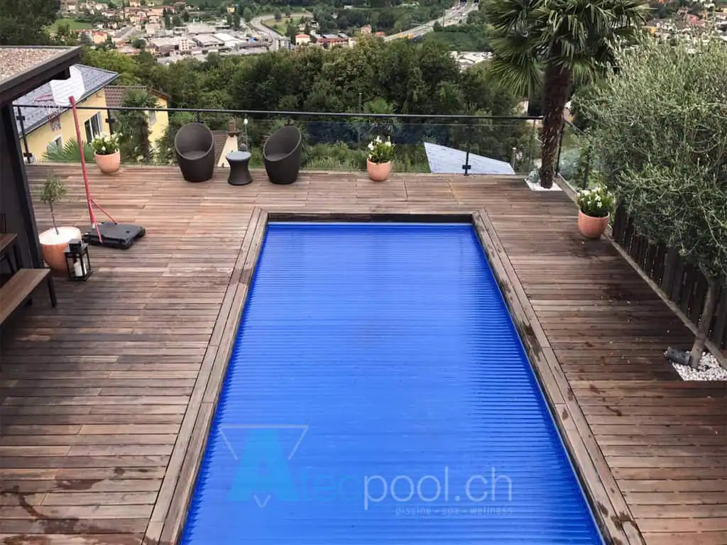 Piscina interrata con copertura a scomparsa in un terrazzo in legno. Atmosfera rilassante con piante e sedie moderne. Vista panoramica sulla natura circostante.