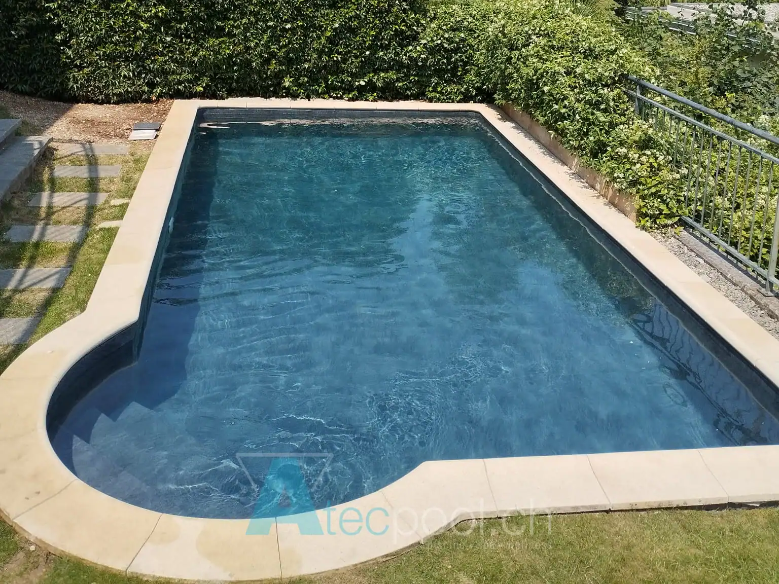 Piscina interrata con rivestimento blu e bordo in pietra naturale in un giardino