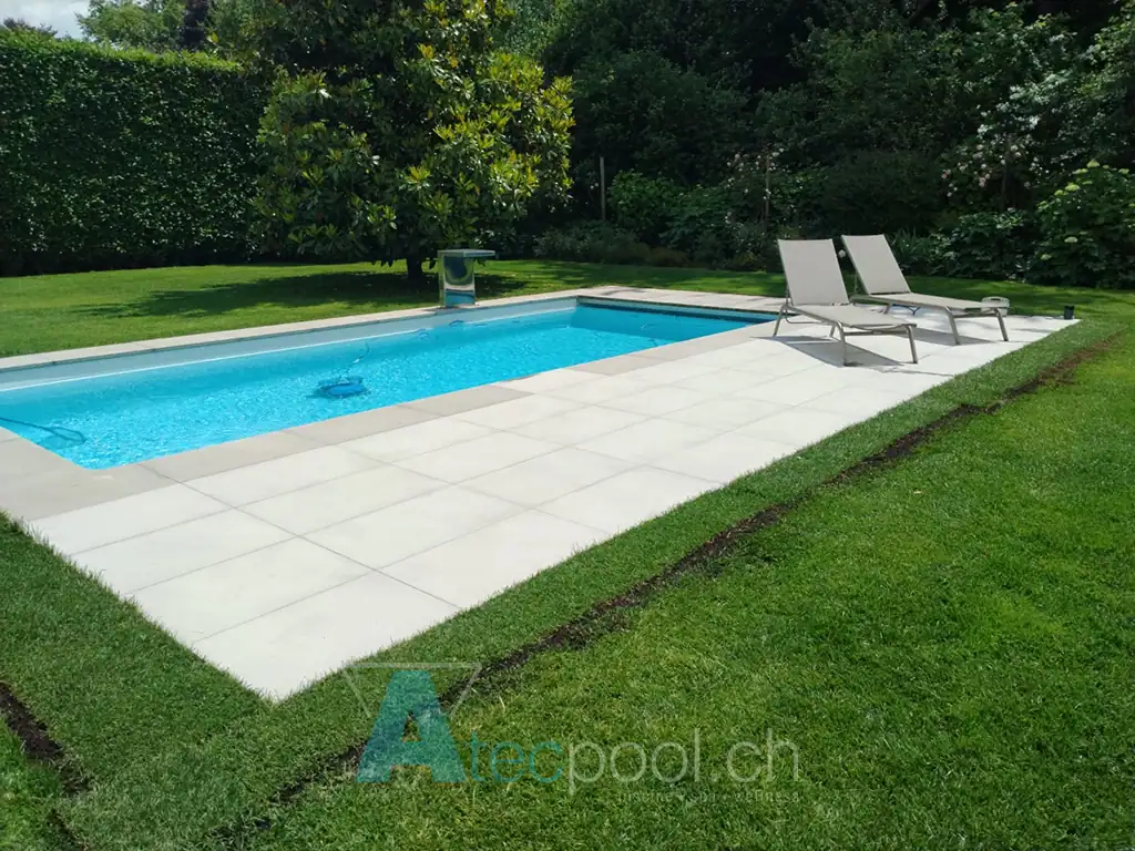 Piscina rettangolare interrata con ampia area prendisole in un giardino verde
