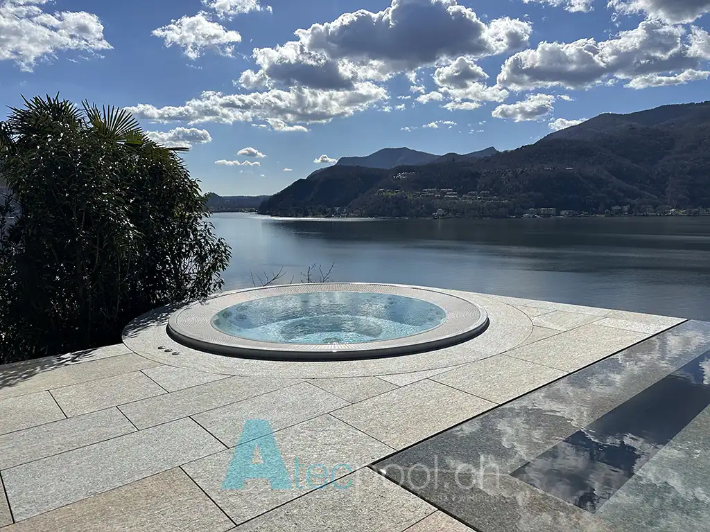 Piscina idromassaggio interrata con vista lago e montagne sullo sfondo.