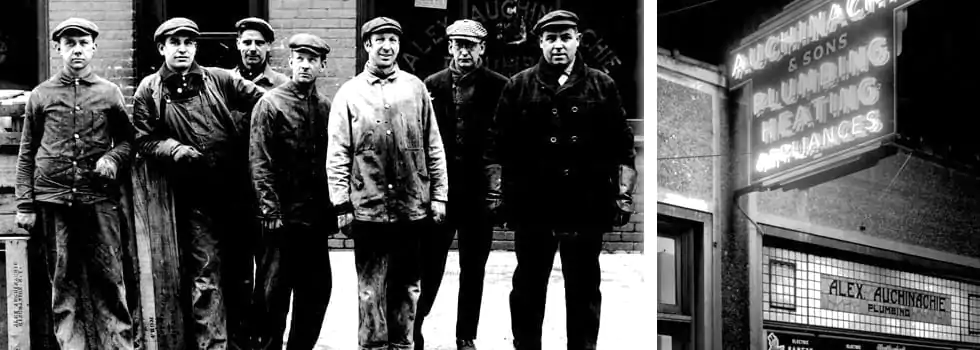A group of six men in work attire stand outside a building. Beside them is a sign displaying "Plumbing Heating Appliances" and "Alex Aichinger & Sons.
