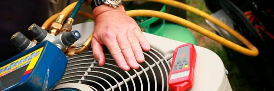 Close-up of a person's hand on an HVAC unit with tools and gauges nearby, including yellow hoses and a red digital device.