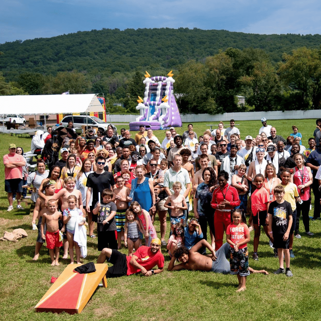 A large group of people pose outdoors on a grassy field with a pink inflatable slide in the background.