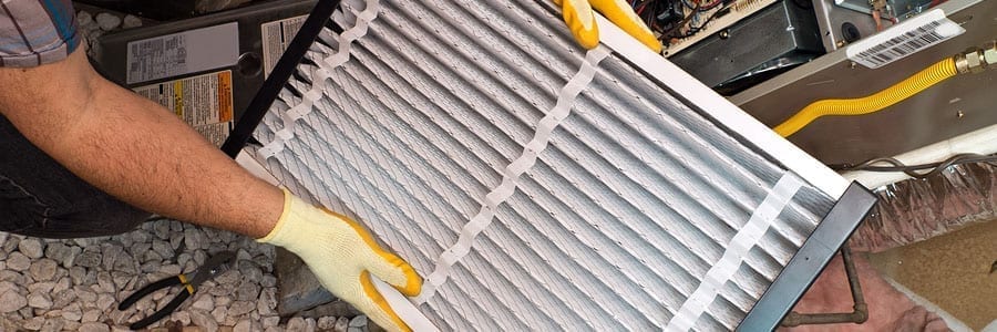 Person wearing gloves replacing an air filter in a heating, ventilation, and air conditioning (HVAC) unit.