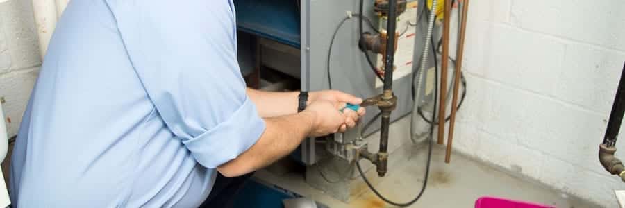 Person adjusting a valve on a water heater in a basement.