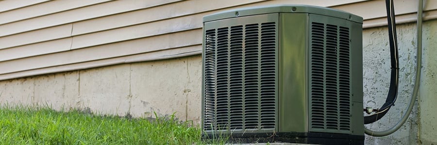 Outdoor air conditioning unit with metal casing next to a house, surrounded by grass.