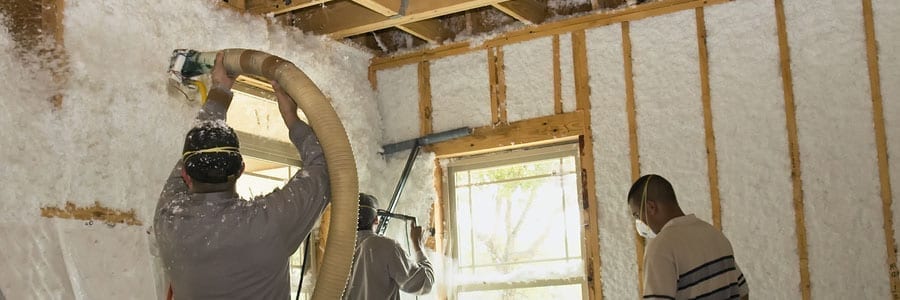 Workers installing spray foam insulation on interior walls of a building under construction.