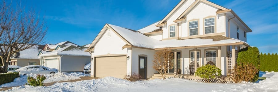 A two-story house with a snow-covered yard and driveway, under a clear blue sky.