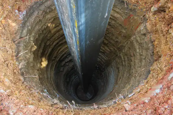 A large pipe is vertically inserted into a deep, circular hole dug in the soil.