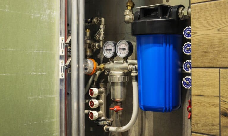 Water filtration system with pressure gauges, pipes, valves, and a large blue filter installed in a utility area.