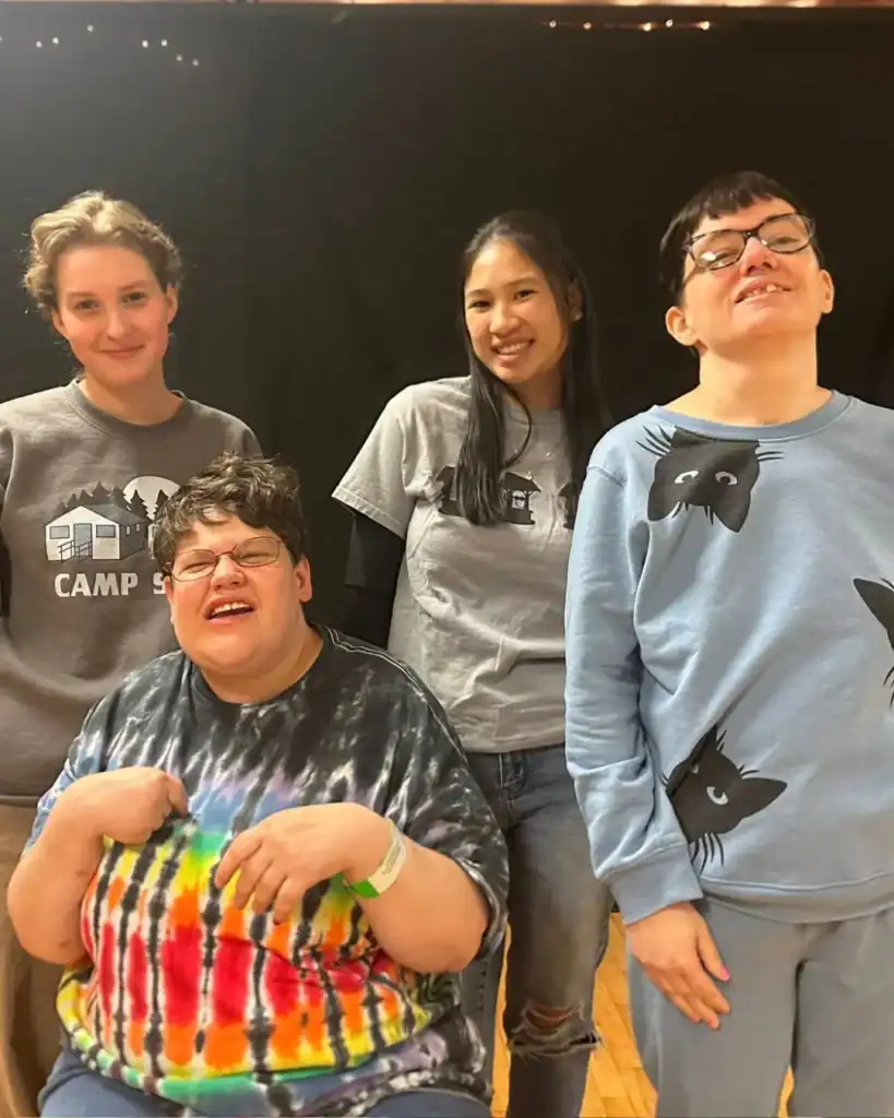 Four people pose and smile together indoors; two are standing in the back and two are in front, one on a chair. They wear casual clothes and appear to be enjoying themselves, showcasing the spirit of Auchinachie Cares.