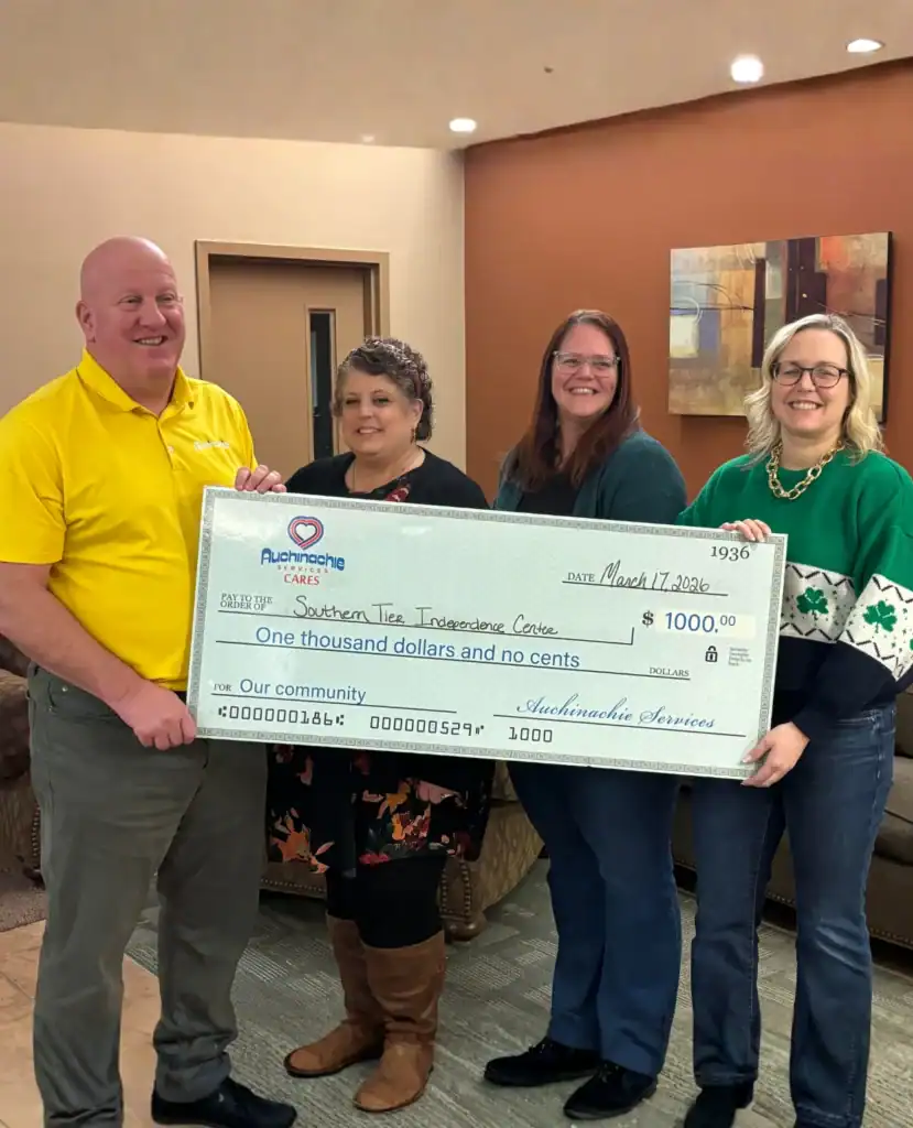 Four people stand indoors holding a $1,000 check made out to Southern Tier Independence Center, dated March 17, 2023, as part of the Auchinachie Cares initiative.