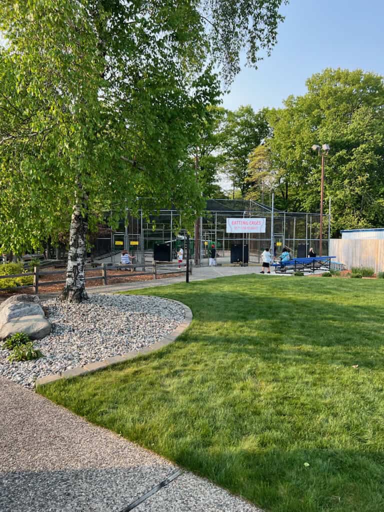 Playground area with construction fencing and equipment, surrounded by trees and grass.