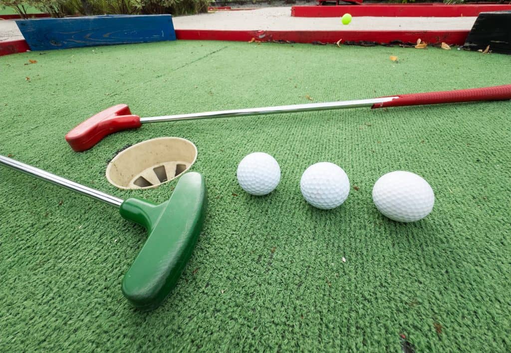 Mini golf putters and balls on artificial turf at the scorecard area.