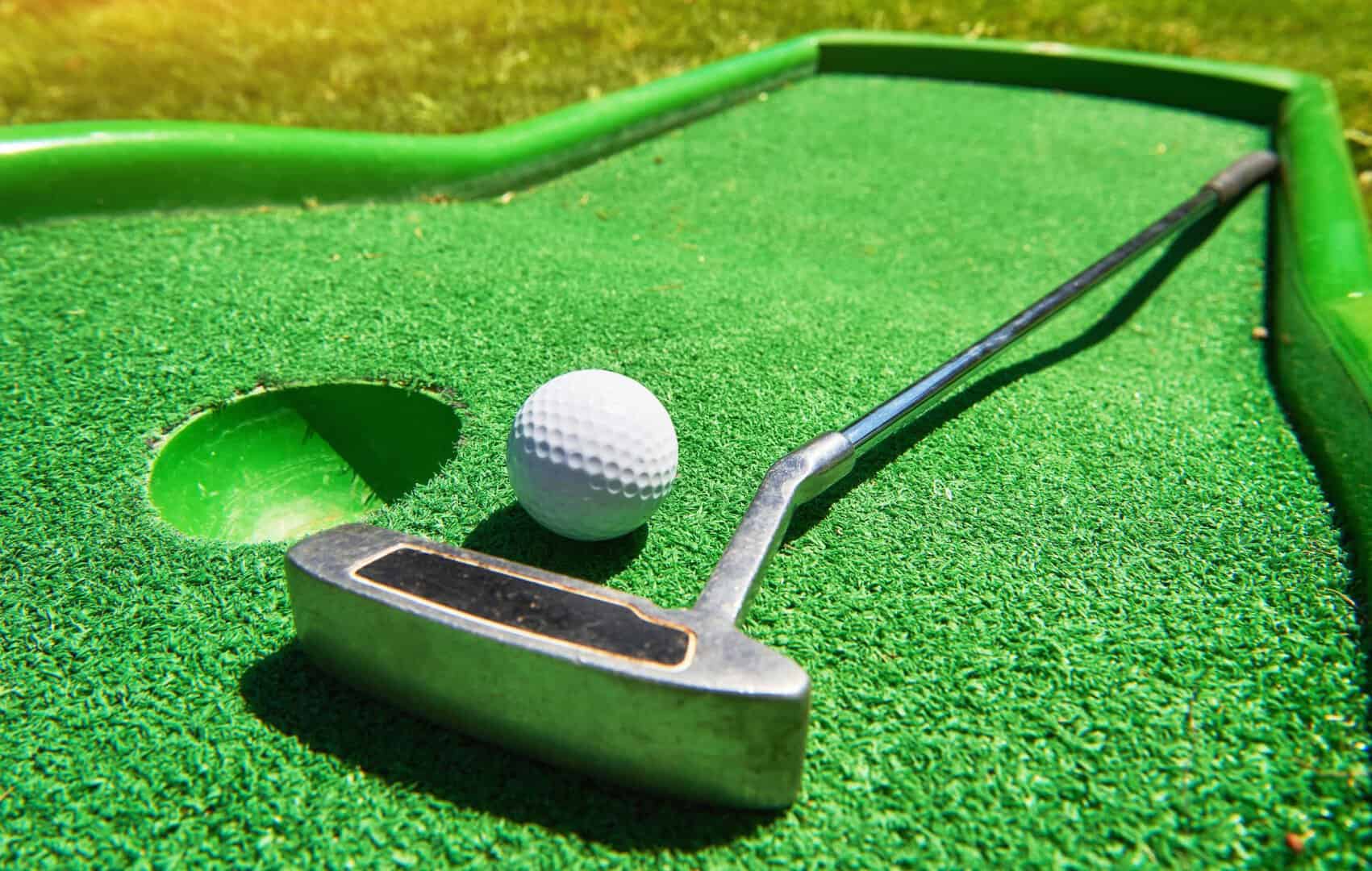 Miniature golf putting green with golf club and ball on synthetic turf for fun outdoor activity.