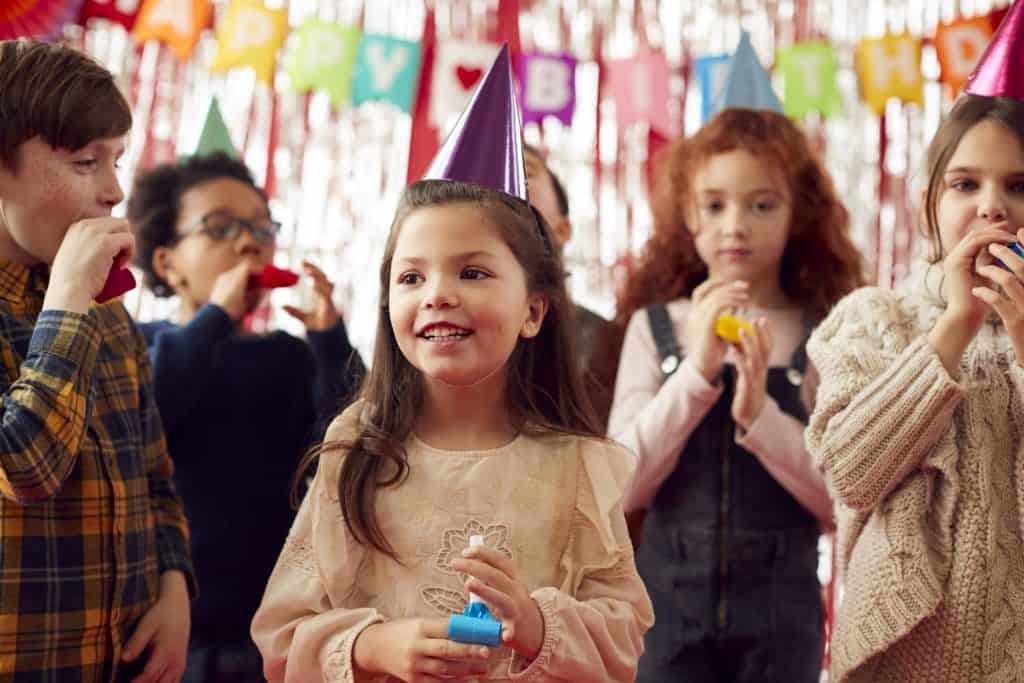 Children celebrating birthday with party hats and snacks at a festive gathering.