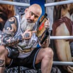 Tattooed man sports a championship belt at boxing event in Aachen.