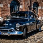 Altes schwarzes Auto vor Ziegelsteinmauer in Aachen, vintage Fahrzeug, historische Autokunst.