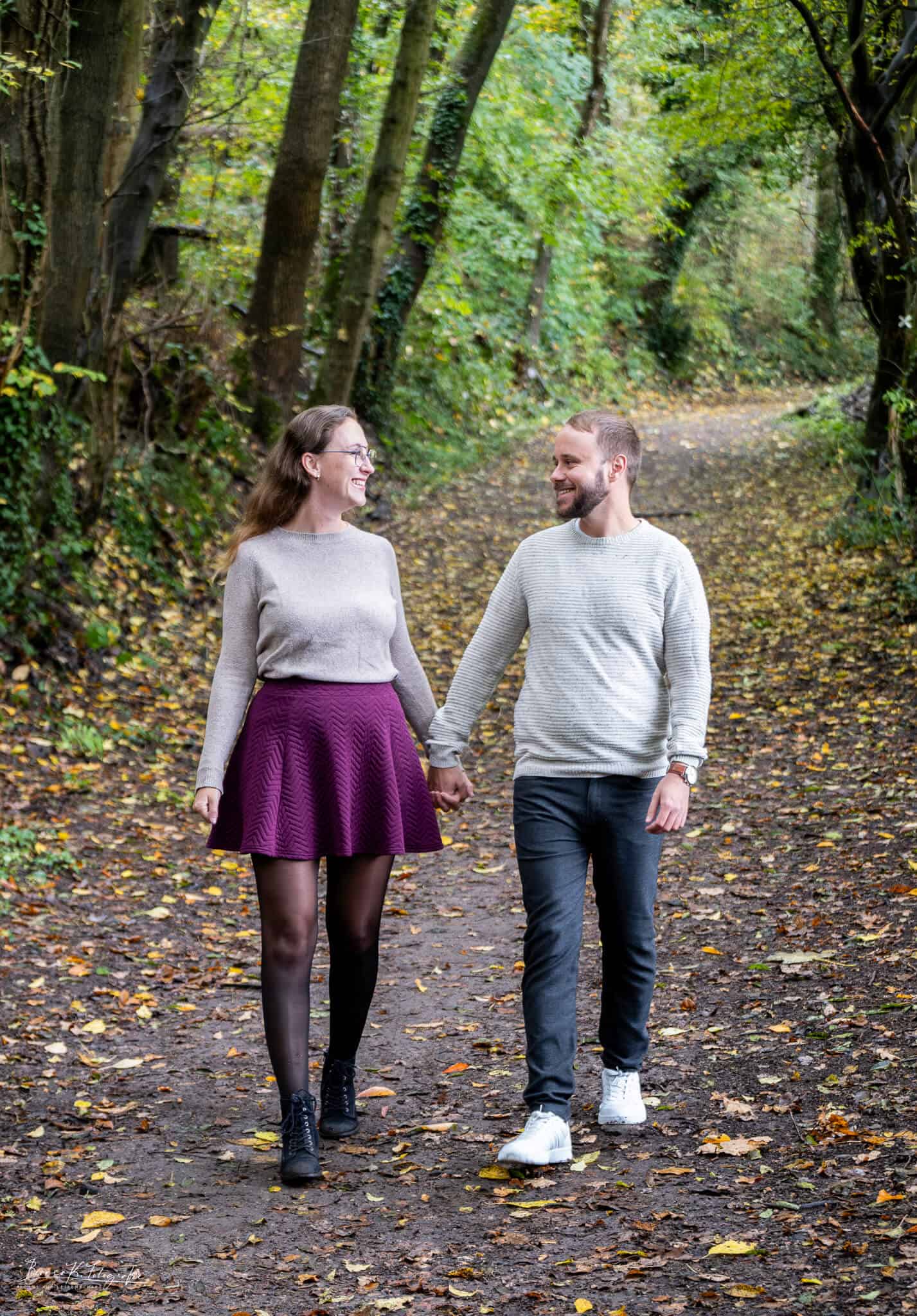 Lächelndes Paar beim Spaziergang im herbstlichen Wald, verliebte Fotos für Hochzeit, Verlobung oder Paarshootings in Aachen. Romantisches Pärchen im Wald, herbstliche Natur, Spaziergang, verliebtes Paar, natürliche Hochzeitsfotografie, Outdoor-Fotoshooting, Paarfotografie, Naturaufnahme, idyllisch, entspannt.