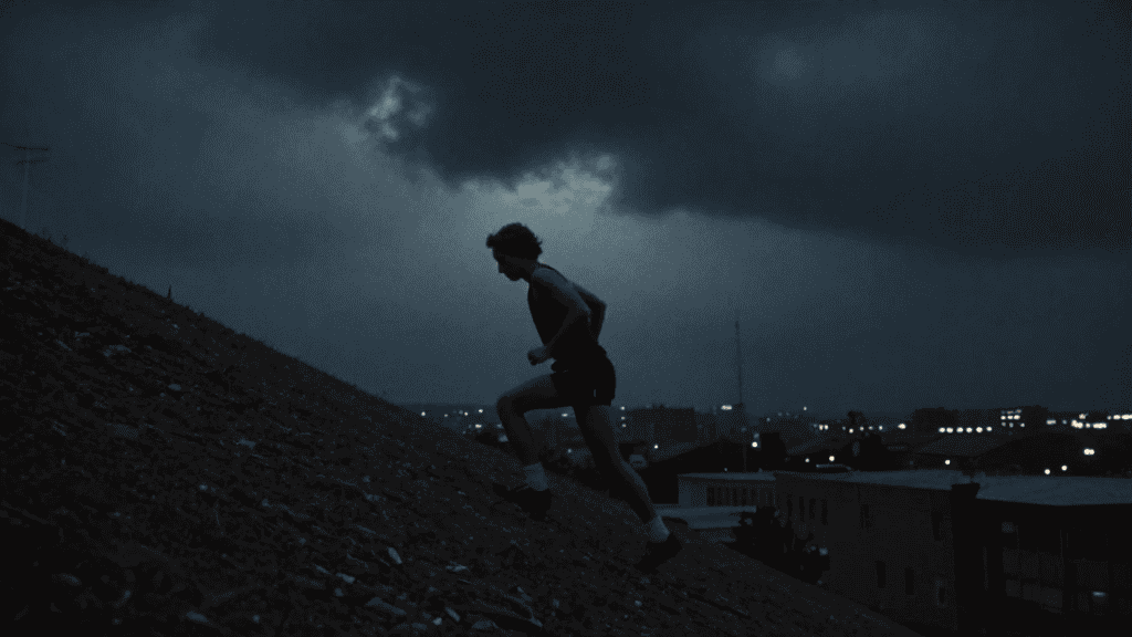 Coureur grimpe une pente raide sur un toit urbain au crépuscule, sous un ciel orageux.