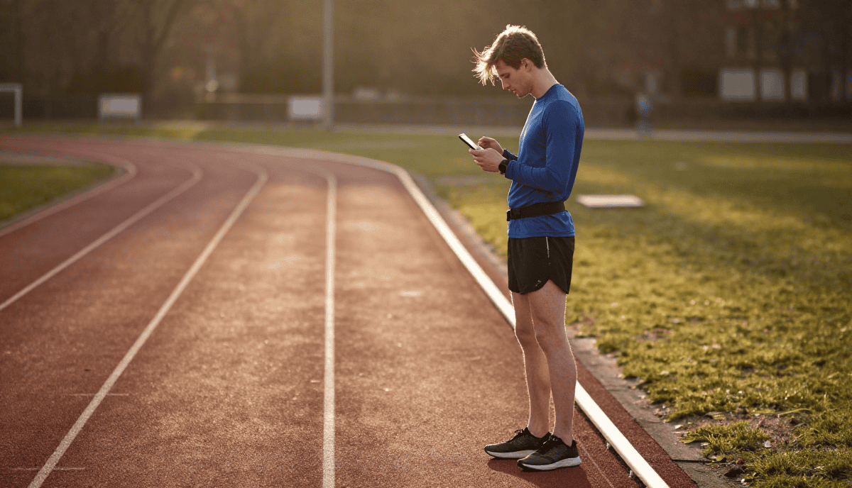 Jeune homme en tenue de sport utilisant un smartphone sur une piste d'athlétisme.