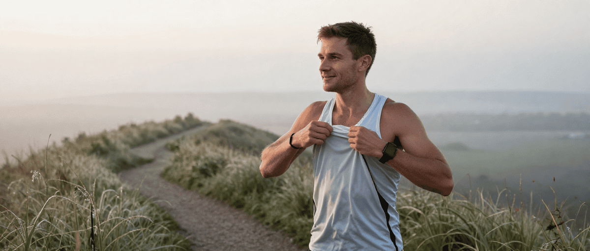 Homme courant en trail dans un paysage naturel au lever du soleil.
