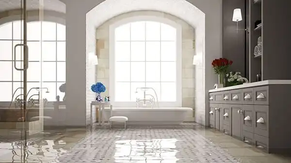 Luxurious bathroom with a flooded floor, featuring a bathtub by a large window, a vanity with drawers, and decorative flowers.