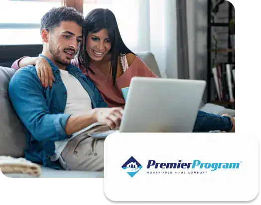 A man and woman sit on a couch looking at a laptop together, with the Premier Pro Program logo and tagline "Worry-Free Home Comfort" displayed in the corner.