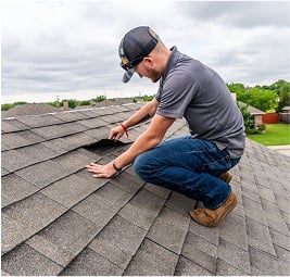 Technician inspecting loose or lifted shingles during a routine roof evaluation on a gray shingle roof.
