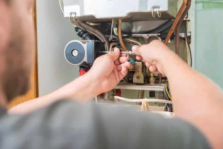 A person uses a wrench to repair or adjust internal components of a wall-mounted boiler or heating system.