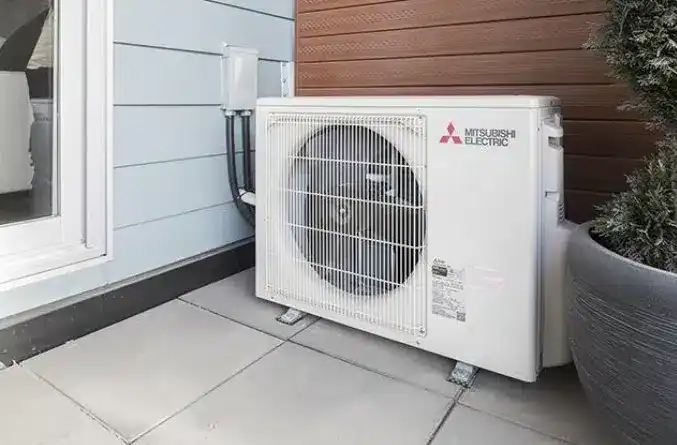 Outdoor Mitsubishi Electric air conditioning unit installed on a patio with light gray tiles next to a building with blue and brown siding.