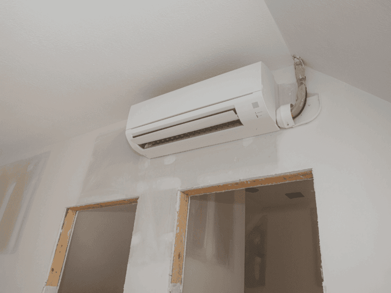 A wall-mounted air conditioning unit is installed above two unfinished door frames in a room with partially completed drywall.