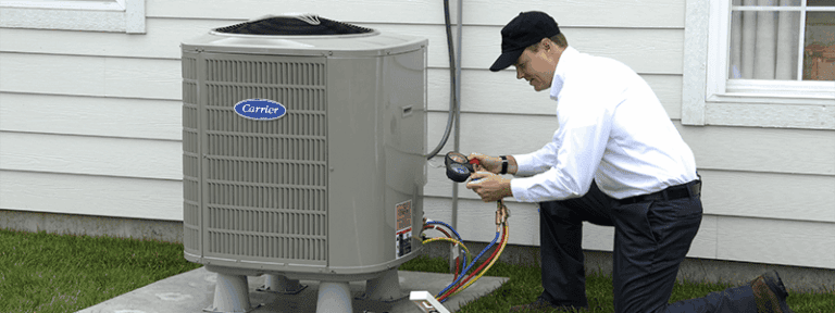 A technician in uniform checks the gauges on an outdoor air conditioning unit beside a house.